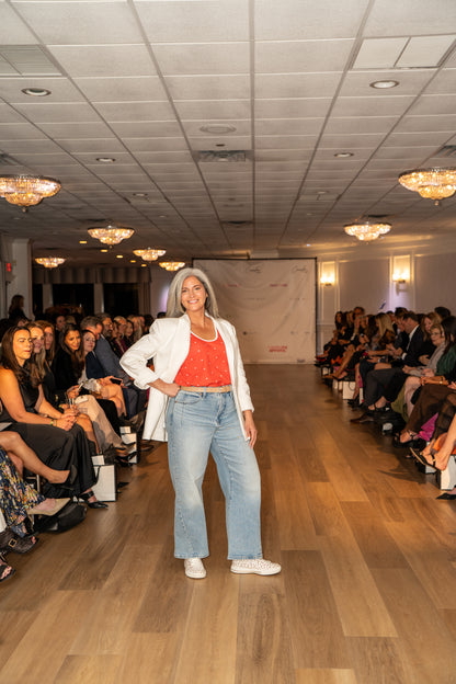 Woman wearing Love Buzz tank top walking on a runway at a fashion show with an audience watching.
