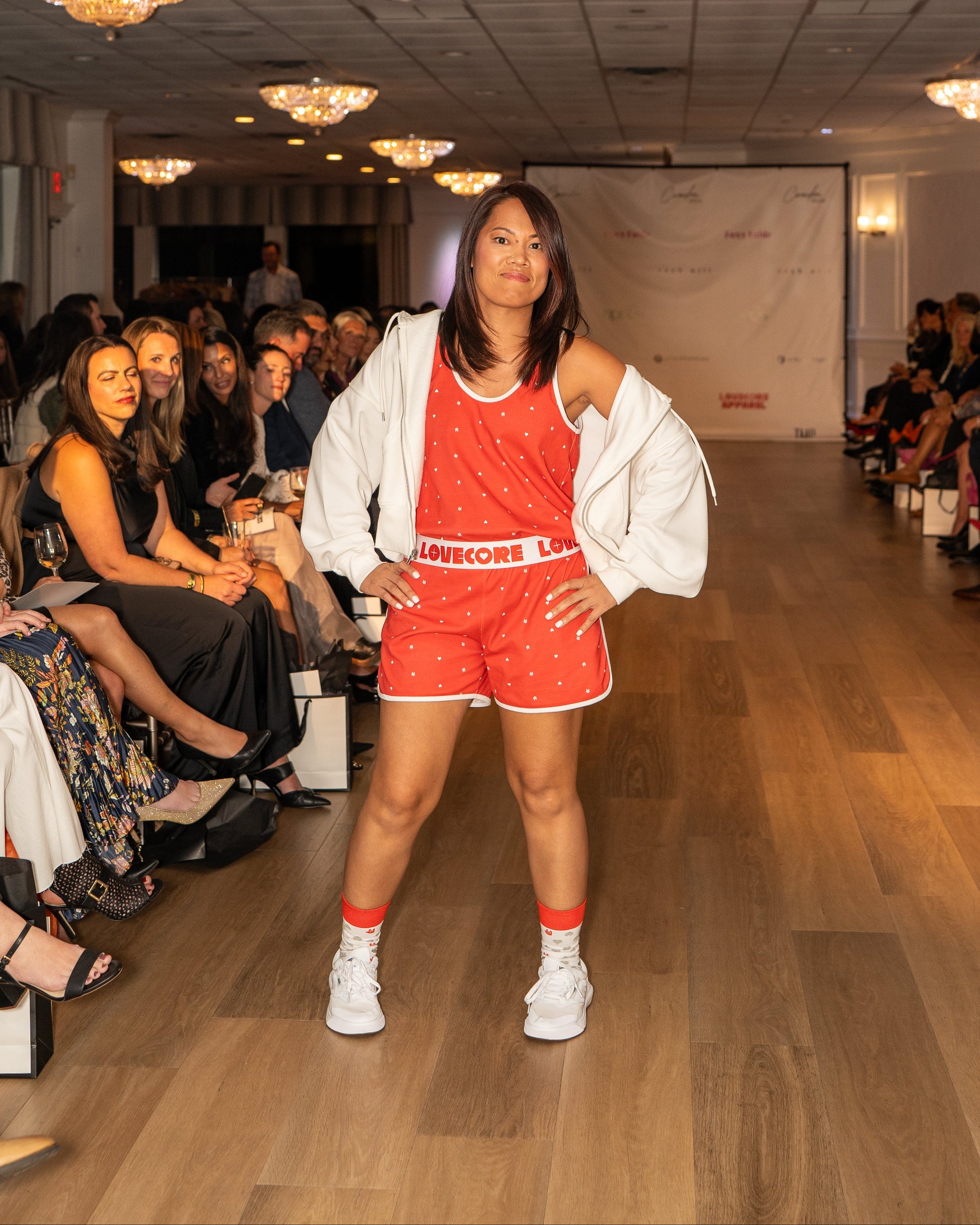 Model in a red outfit set with 'LOVECORE' branding on a runway with an audience.