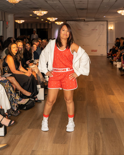 Model in a red outfit set with 'LOVECORE' branding on a runway with an audience.