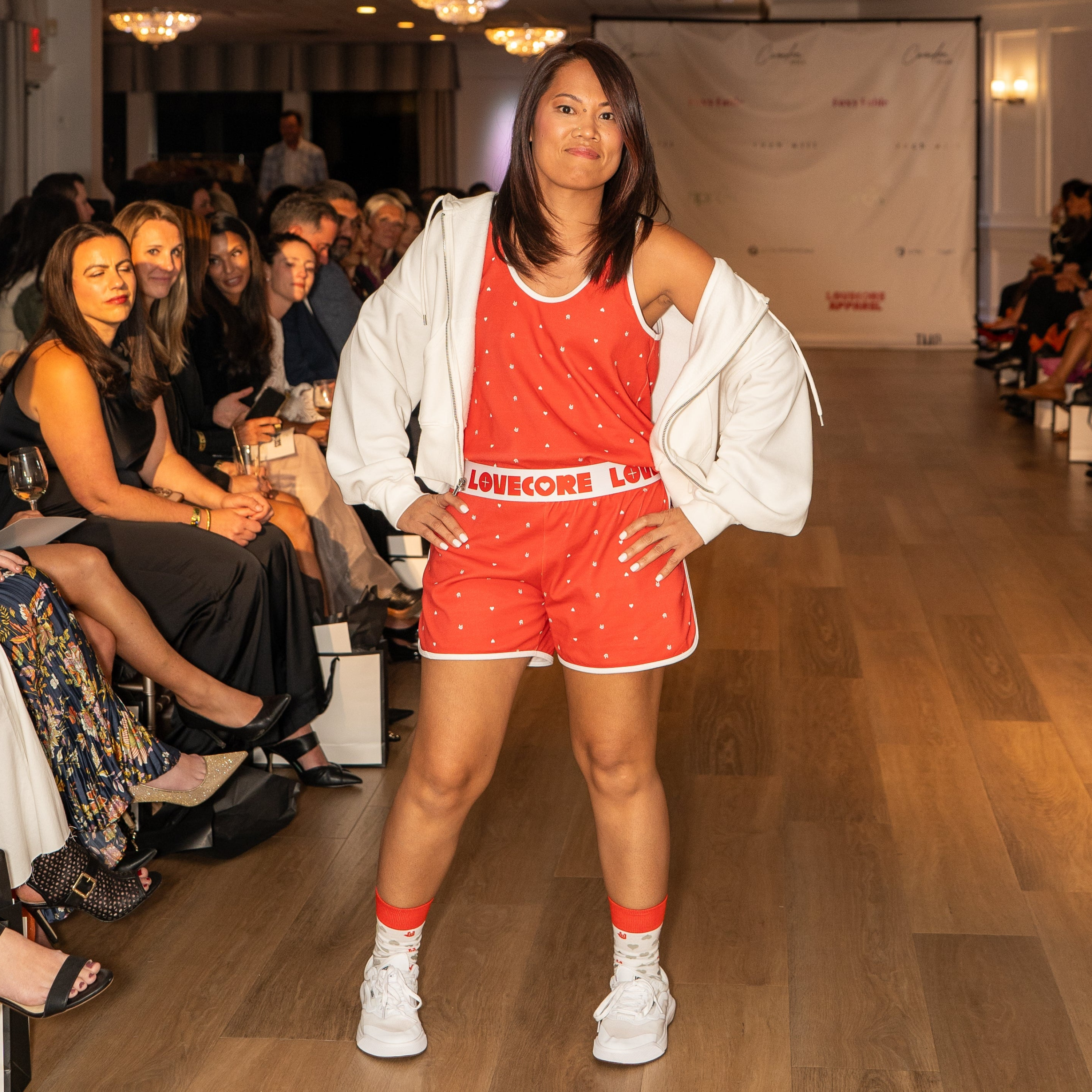 Model in red outfit with 'LOVECORE' text on a runway at a fashion event.