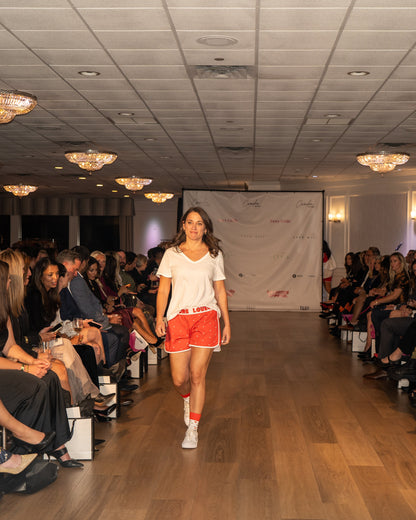 Model wearing Love Buzz shorts walking down a runway at a fashion event with an audience on either side.