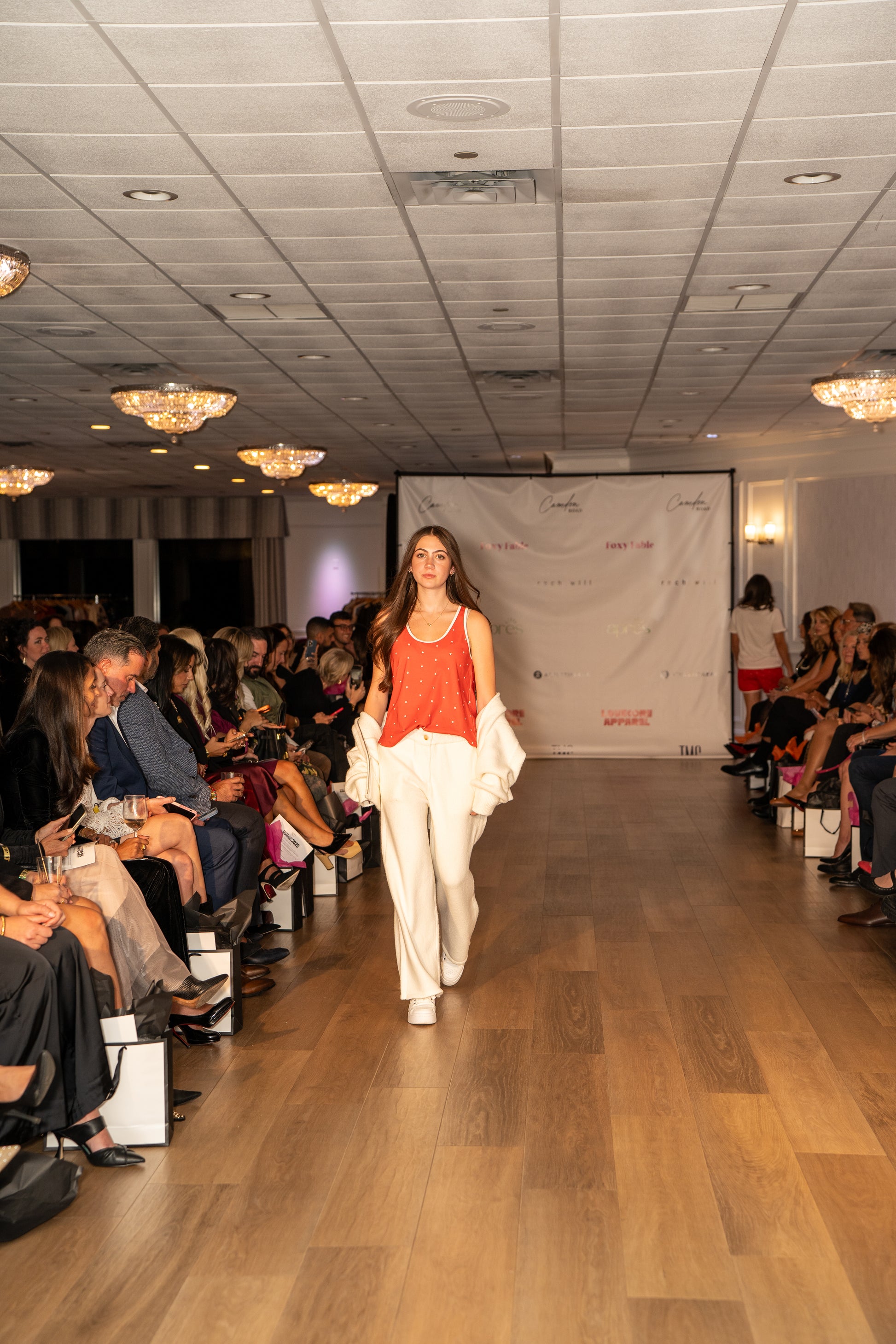 Model wearing Love Buzz tank top walking down a runway at a fashion show with an audience on either side.